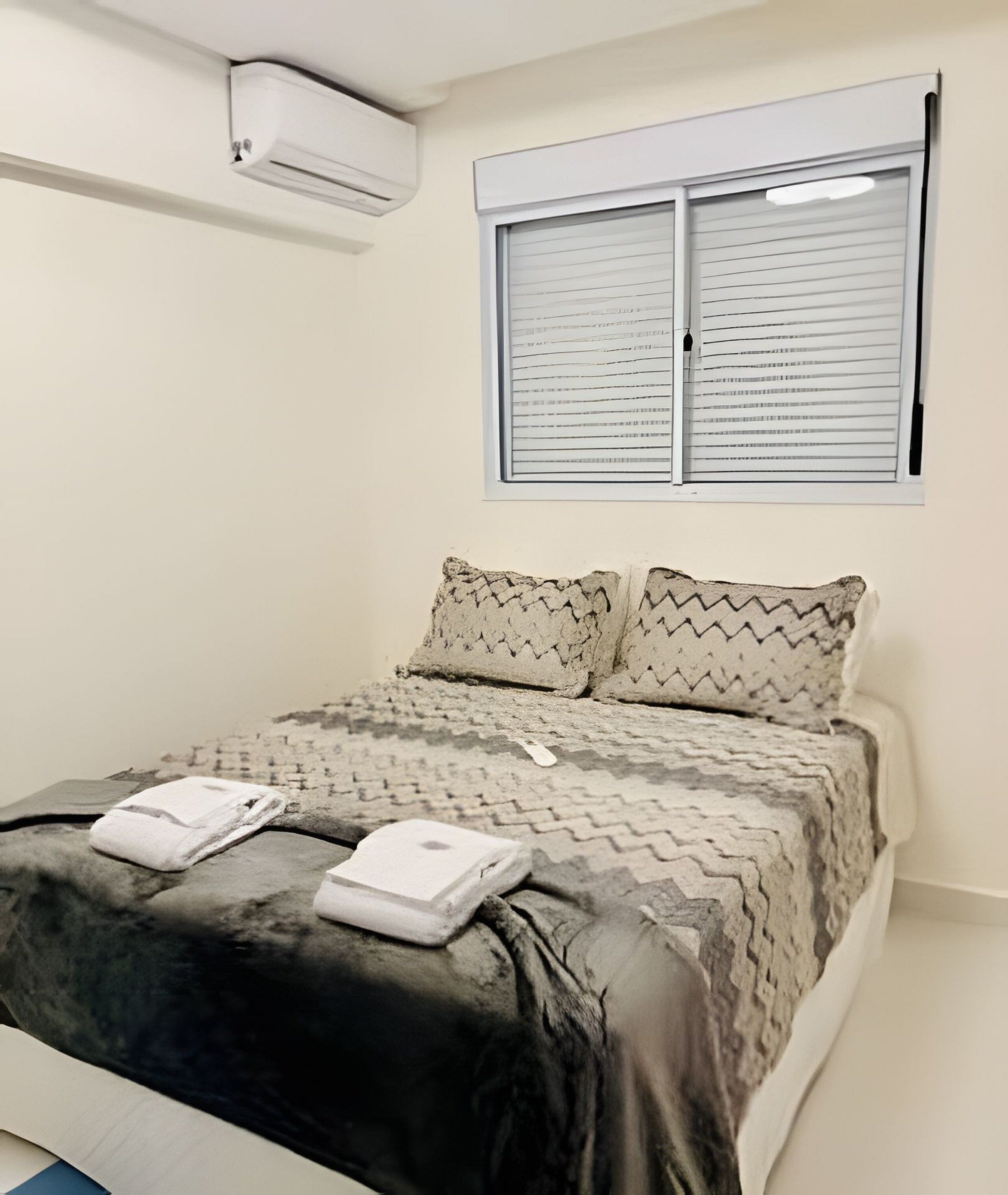 Une chambre à coucher avec un lit, des oreillers, une couverture et une fenêtre avec des stores.