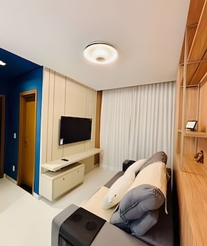 A modern hotel room with a bed, a TV mounted on a wall, a wooden cabinet, and a door leading to another room. - 1501 Apto2 Qtos Vista Mar (Cabedelo)