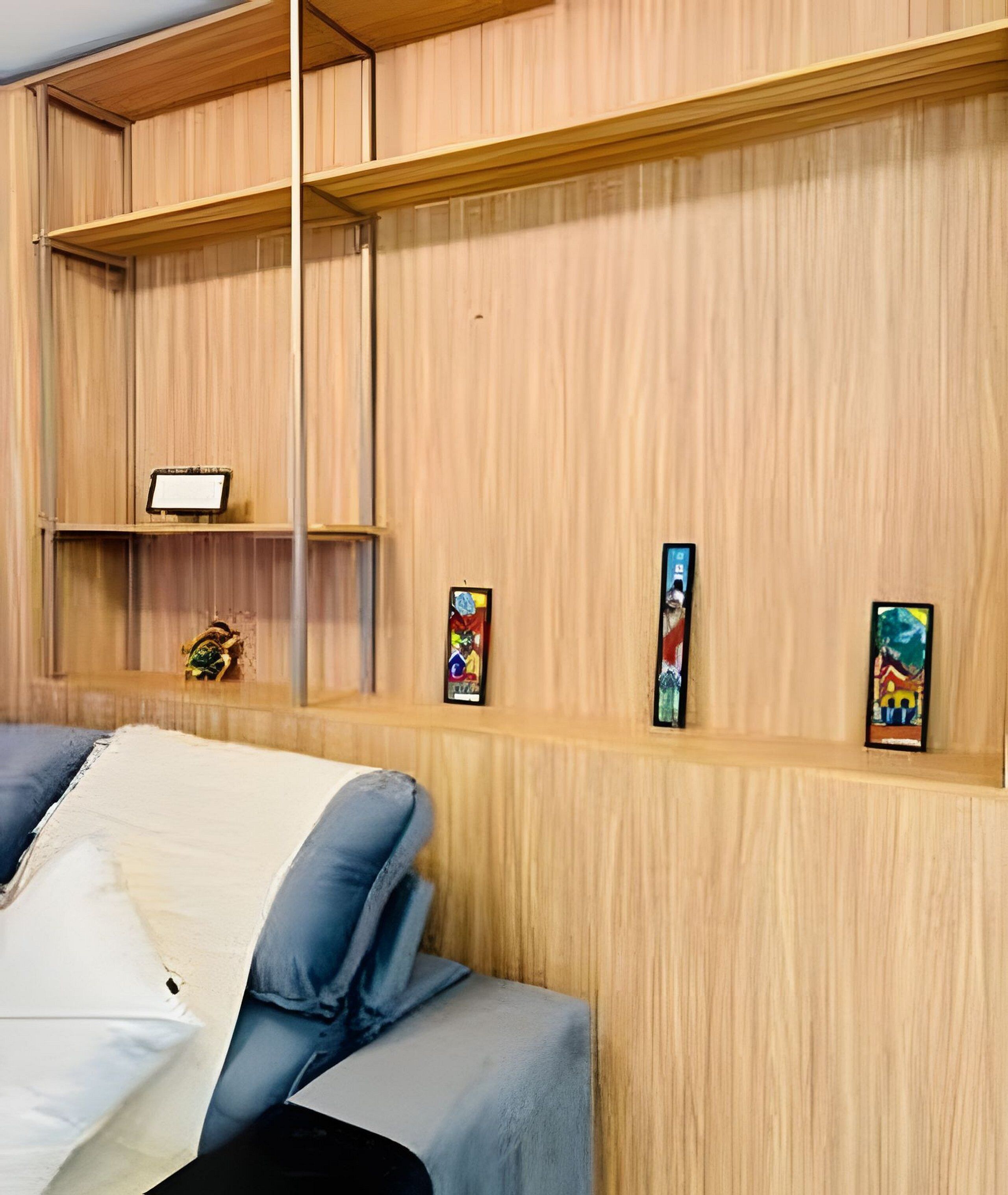 A room with a bed, a wooden shelf with artwork, and a small table with a lamp.