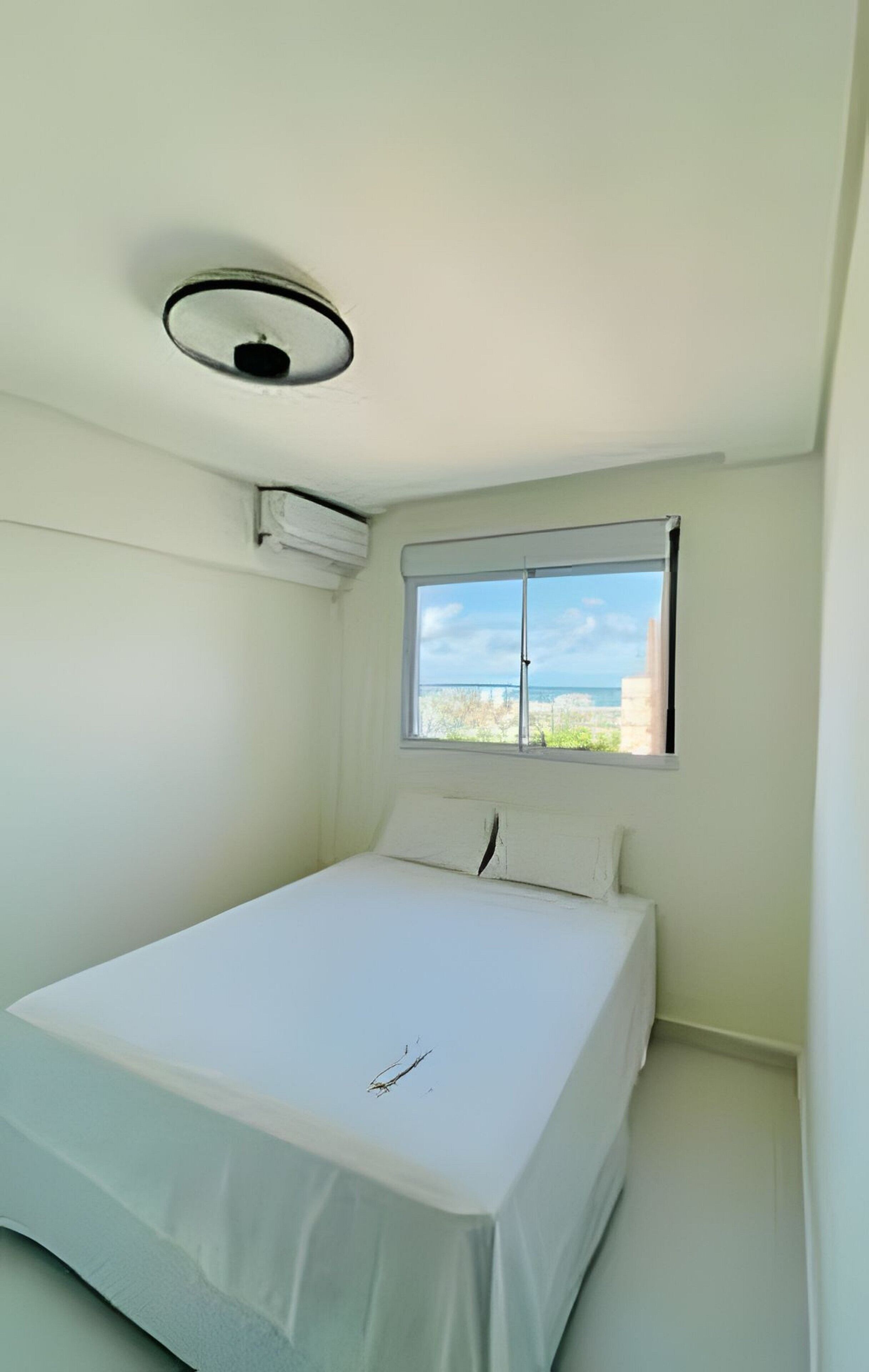 Una habitación pequeña y limpia con una cama, una ventana con vistas y una lámpara en el techo.