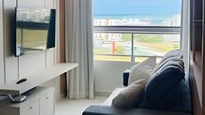 Un dormitorio moderno con televisor, sofá y un amplio ventanal con vistas al mar.