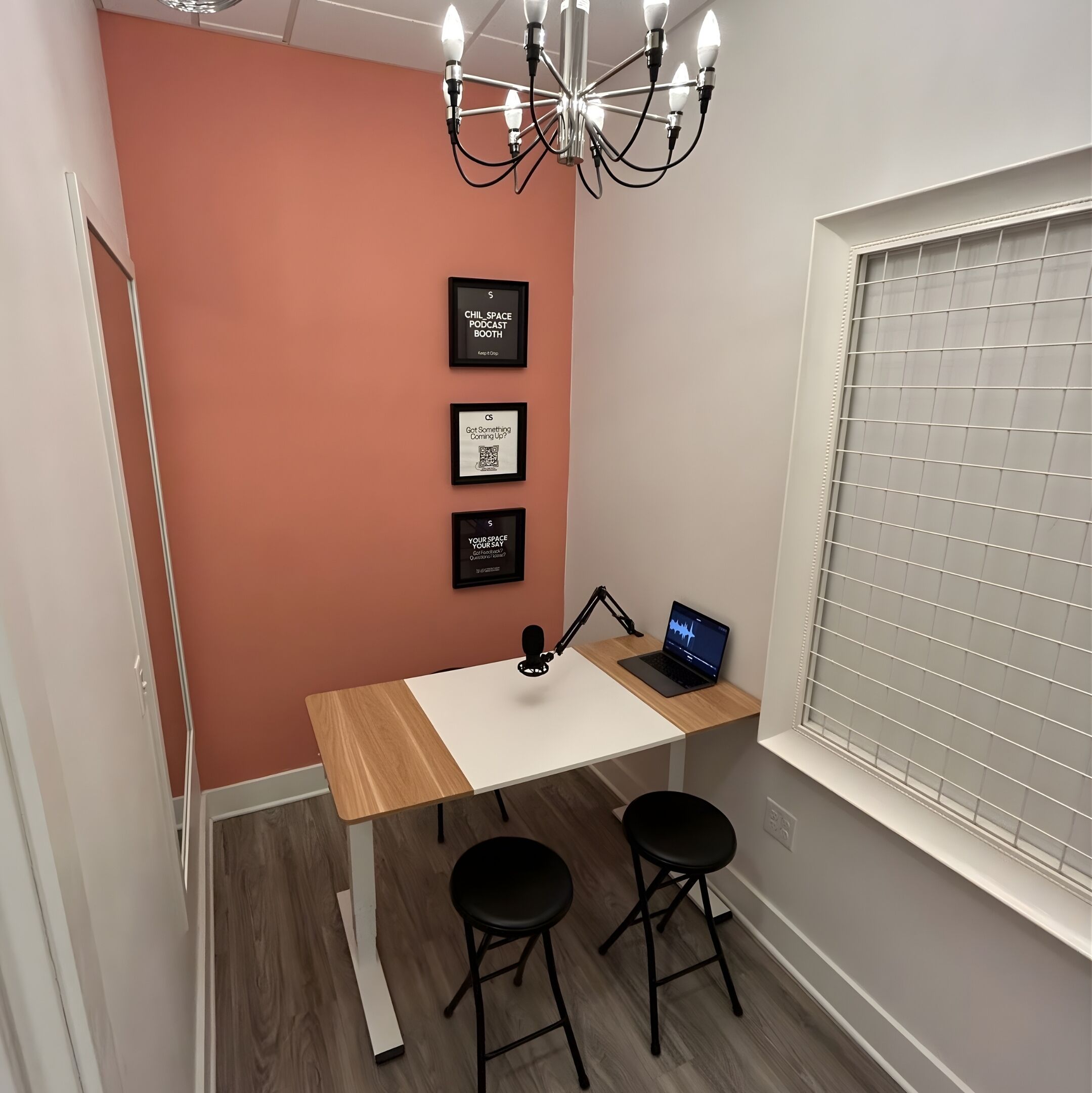 Un espacio de trabajo pequeño con un escritorio, dos sillas, una computadora portátil e iluminación instalada en la pared.