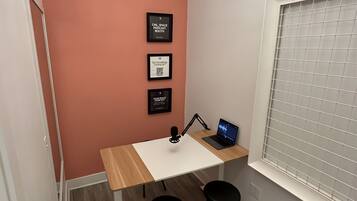 A small workspace with a desk, two chairs, a laptop, and a wall-mounted light fixture.