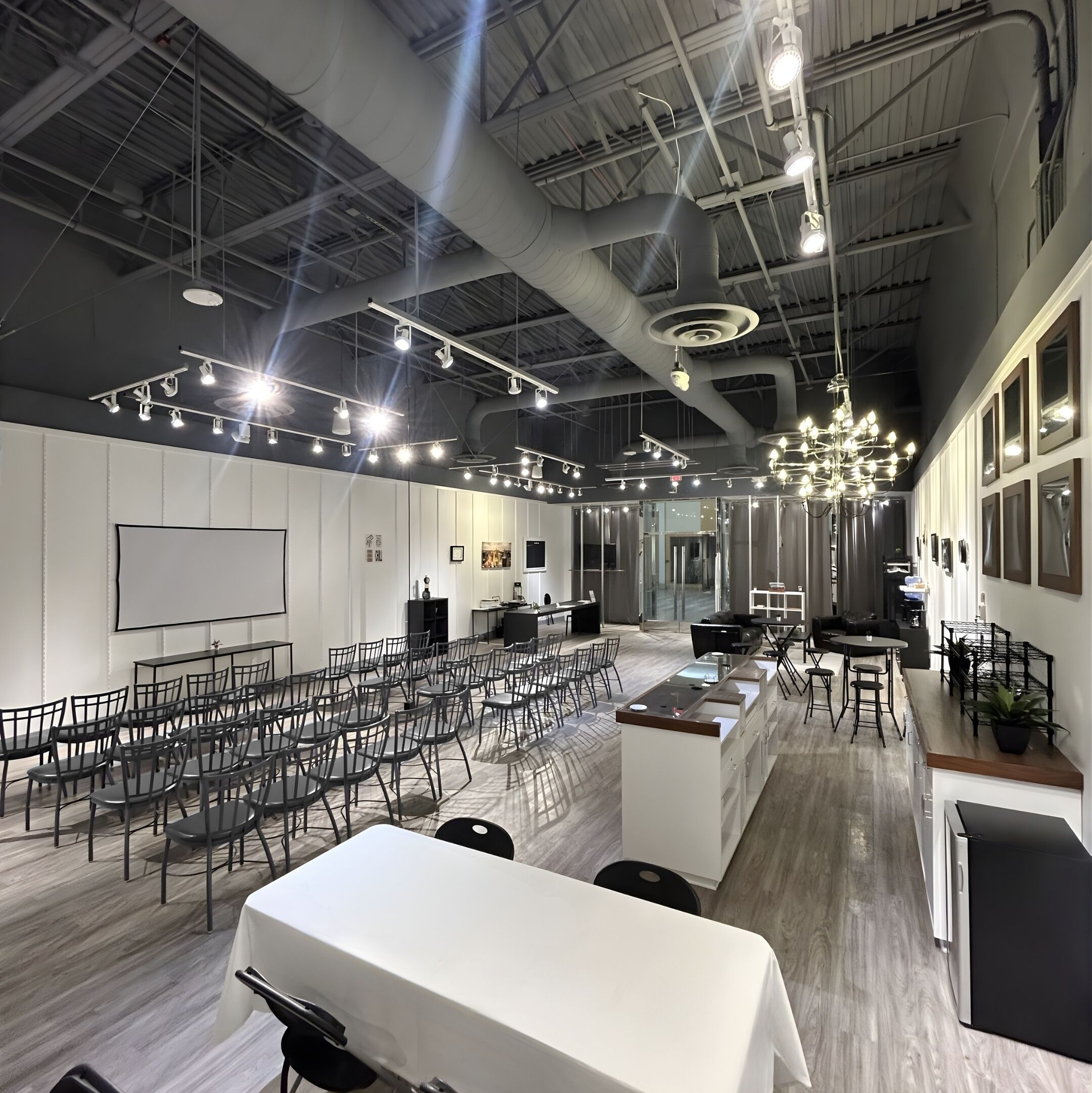 Una amplia sala de conferencias con filas de sillas, una pizarra blanca y una zona de cocina con mostrador y taburetes.