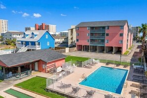 A hotel with a swimming pool, outdoor seating, and a red building. - Gulf Shores - Village by the Gulf 2/2 balcony (Gulf Shores)