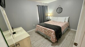 A bedroom with a bed, a bedside table, a lamp, and a mirror on the wall. - Gulf Shores - Village by the Gulf 2/2 *balcony* (Gulf Shores)