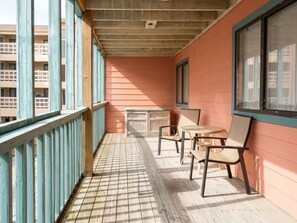 A balcony with a wooden floor, a table, and two chairs. - Gulf Shores - Village by the Gulf 2/2 balcony (Gulf Shores)