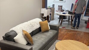 Een moderne woonkamer met een grijze bank, een ronde houten salontafel en een kamerbreed tapijt met een patroon.