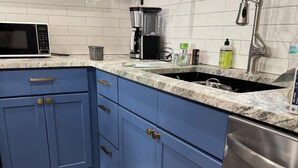Een keuken met blauwe kastjes, een roestvrijstalen vaatwasser, een magnetron, een koffiezetapparaat en een spoelbak met kraan.