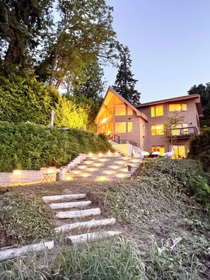 A modern two-story house with a wooden exterior, a stone staircase leading to the entrance, and a well-maintained garden.