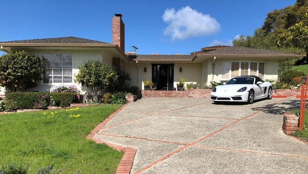 A house with a driveway leading to a white sports car parked in front.