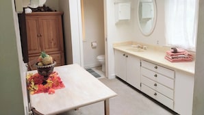 A bathroom with a sink, mirror, and toilet. There is a wooden cabinet and a table with a pineapple and leaves.