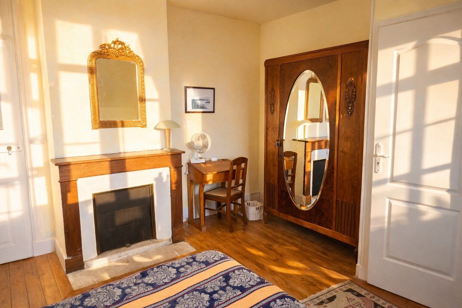 Una habitación con chimenea, un armario de madera con espejo, un escritorio y una silla, y una alfombra estampada.