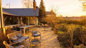 Een terras buiten met stenen vloer, rieten meubels en een eettafel.