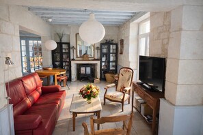 Una sala de estar acogedora con un sofá de cuero rojo, una mesa de centro de madera con un centro de flores, un sillón de madera y un televisor sobre un mueble de madera.