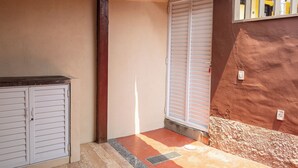 A corner of a room with a white door, a window with white shutters, and a red wall. - Apartment in downtown Búzios | 2 bedrooms | Air conditioning (Armação dos Búzios)