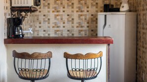 A kitchen with a microwave, coffee maker, and refrigerator. There are two metal chairs with wooden seats. - Apartment in downtown Búzios | 2 bedrooms | Air conditioning (Armação dos Búzios)