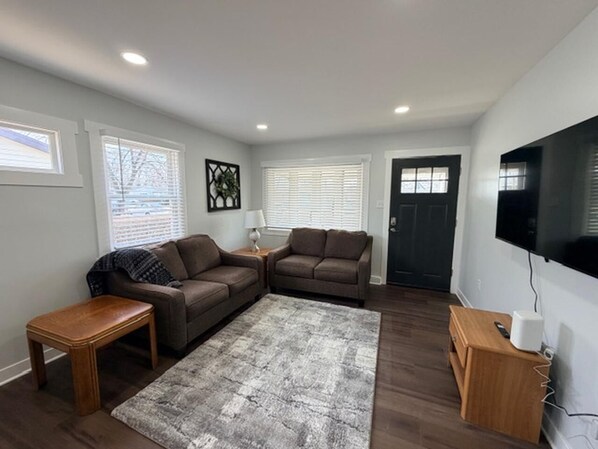 Ein Wohnzimmer mit zwei braunen Sofas, einem Holztisch, einem grauen Teppich und einem an der Wand montierten Flachbildfernseher.