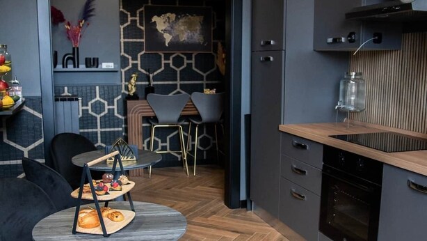 A modern kitchen with dark cabinetry, a wooden countertop, and a built-in oven. There are two black chairs and a round table with a heart-shaped bowl. - ART ROOM One of one Experiences (Rome)