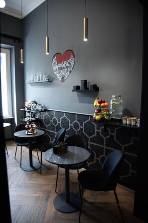L’intérieur d’un café moderne, avec des tables rondes, des chaises noires, un mur orné d’un motif hexagonal et une œuvre d’art en forme de cœur.