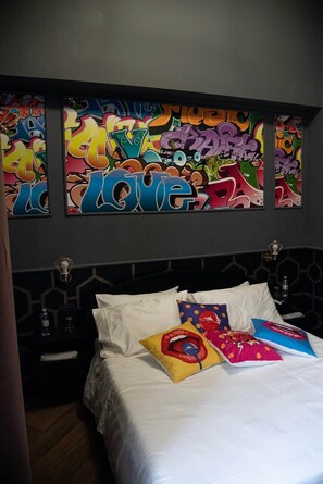 Une chambre d’hôtel avec un lit, du linge de lit blanc et des oreillers colorés.
