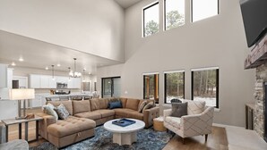 Un salón espacioso con un sofá modular grande, una mesa de centro redonda y una chimenea. Se ve una cocina al fondo con armarios blancos y un comedor.