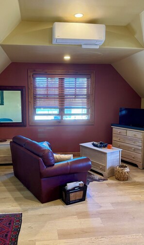 A living room with a leather sofa, a television, a wooden dresser, and a window with blinds. - Centrally located, bright studio next to the bike path in downtown Hailey (Hailey)