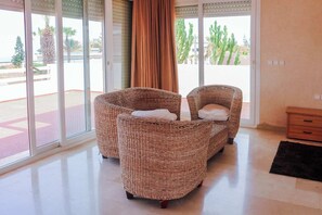 A room with wicker furniture, a sliding glass door, and a view of cacti and palm trees.