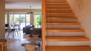 Un intérieur moderne avec un escalier en bois, un coin repas comprenant des chaises et une table, et une vue sur l’extérieur.