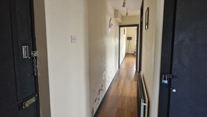 A narrow hallway with a wooden floor, white walls, and a black door on the right. - Apartment in the Heart of Wimbledon  Parking Included! (London)