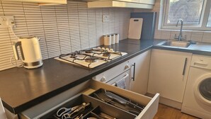 A modern kitchen with a gas stove, a kettle, a dishwasher, and a drawer organizer with utensils. - Apartment in the Heart of Wimbledon  Parking Included! (London)
