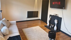 A modern living room with a sofa, a coffee table, a TV mounted on the wall, and a fireplace. - Apartment in the Heart of Wimbledon  Parking Included! (London)