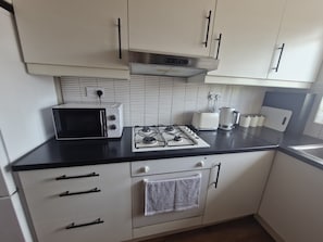 A kitchen with white cabinets, a black countertop, a microwave, a gas stove, and a kettle.