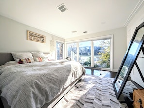 A bedroom with a large bed, a view of the outdoors through a sliding glass door, and a framed picture on the wall.