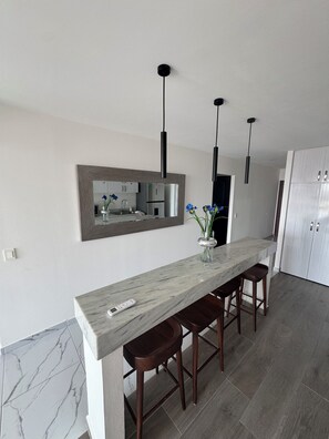 Eine moderne Küche mit Marmorarbeitsplatte, zwei Barhocker, einem eingebauten Backofen und einem großen Spiegel.