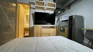 A compact bedroom with a bed, built-in TV, wooden cabinets, and a kitchenette. - Helena Building 1BR ✔️ Breakfast + Jacuzzi + WiFi (Medellín)