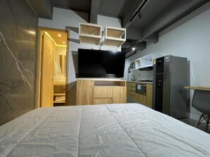 A compact bedroom with a bed, built-in TV, wooden cabinets, and a kitchenette. - Helena Building 1BR ✔️ Breakfast + Jacuzzi + WiFi (Medellín)