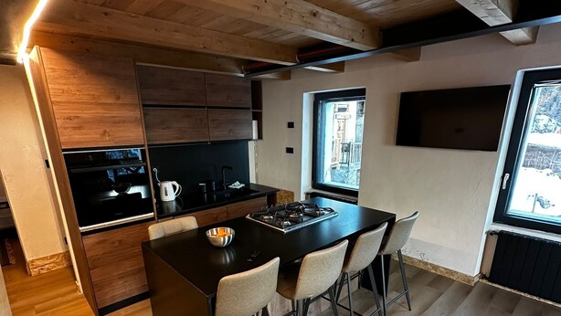 A modern kitchen with wooden cabinetry, a central island with chairs, and a large window providing natural light. - Muranche loft S1, fined and elegant apartment with Jacuzzi (Pâquier)