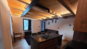 A modern kitchen with a central island, wooden beams on the ceiling, and a dining area with a table and chairs. - Muranche loft S1, fined and elegant apartment with Jacuzzi (Pâquier)
