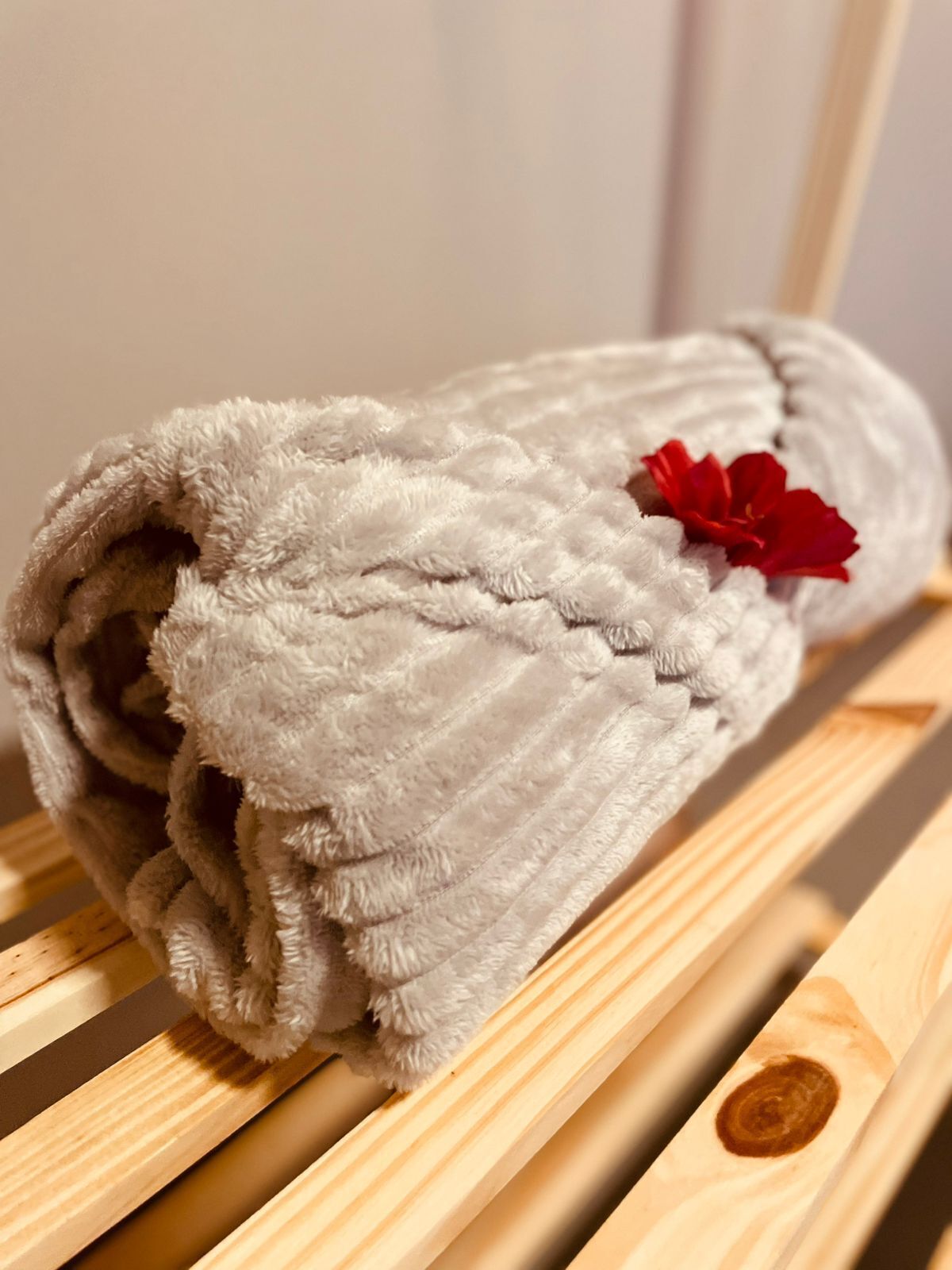 A rolled-up white towel with a red flower on a wooden bench.
