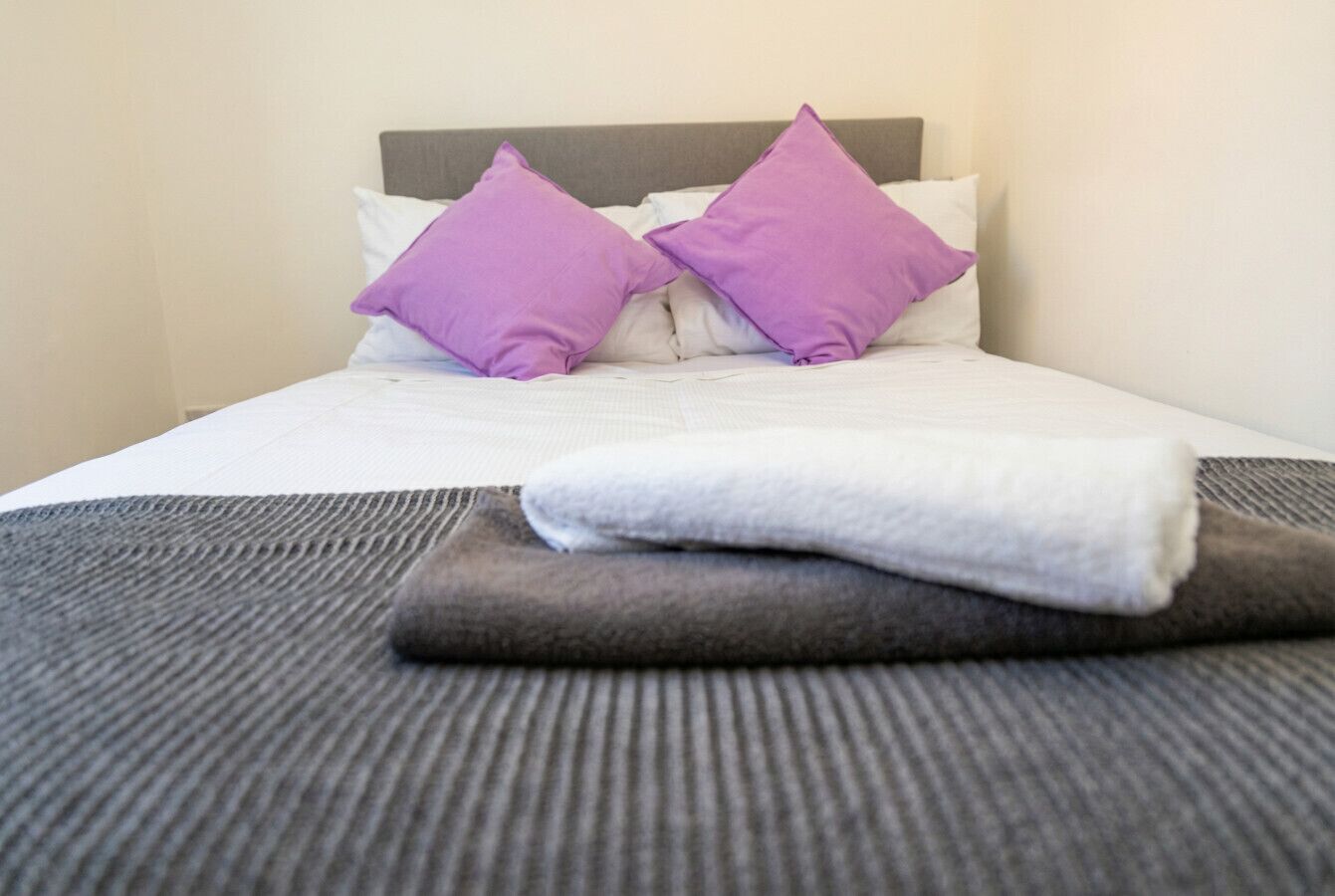 A neatly made bed with a grey blanket and two purple pillows.