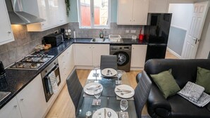 A compact kitchen with a dining area, a black sofa, and a washing machine.
