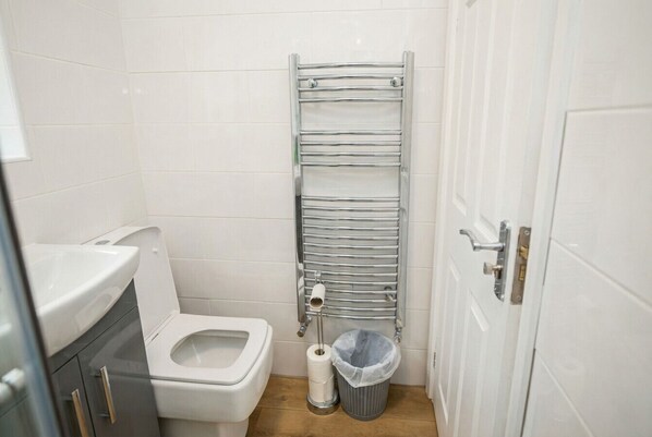 A small, clean bathroom with a toilet, a sink, a towel rack, and a trash bin.