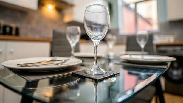 A dining table with a glass top, plates, cutlery, and wine glasses.