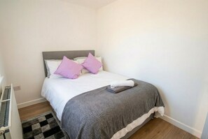 A neatly made bed with a grey headboard, white and grey bedding, and a black and white rug. - Two-bedroom base with wifi, Ethernet and easy access (Openshaw)