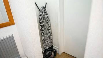 A corner of a room with a zebra-striped item hanging on the wall, a radiator, and a vacuum cleaner on the floor.