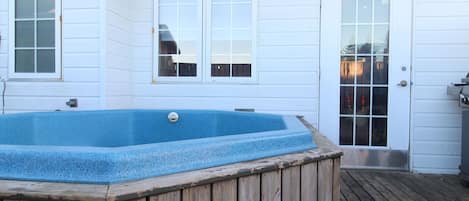 A wooden deck with a hot tub and a white house with a door and windows.