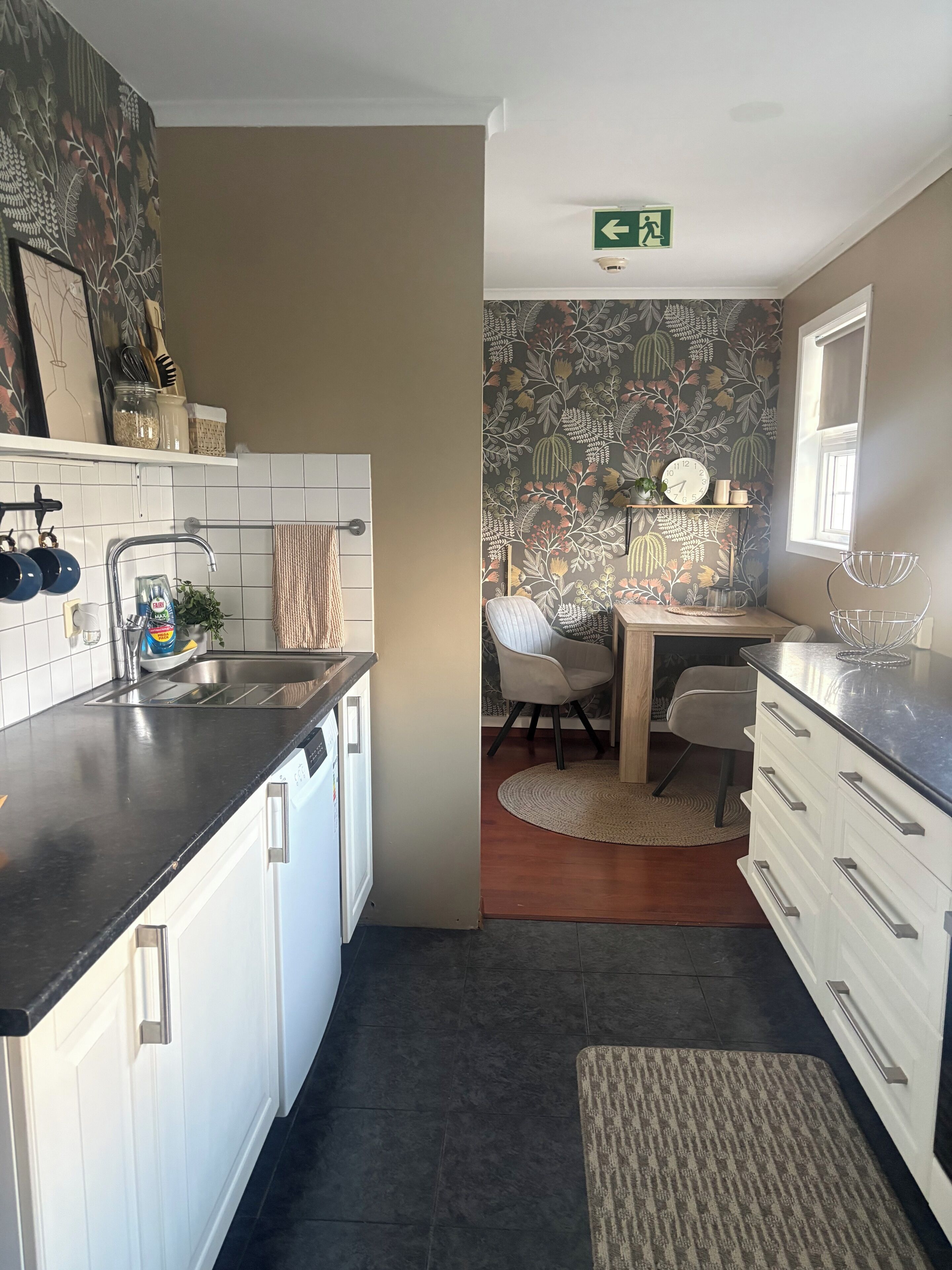 Cocina compacta con armarios blancos, encimera negra y salpicadero de azulejos.