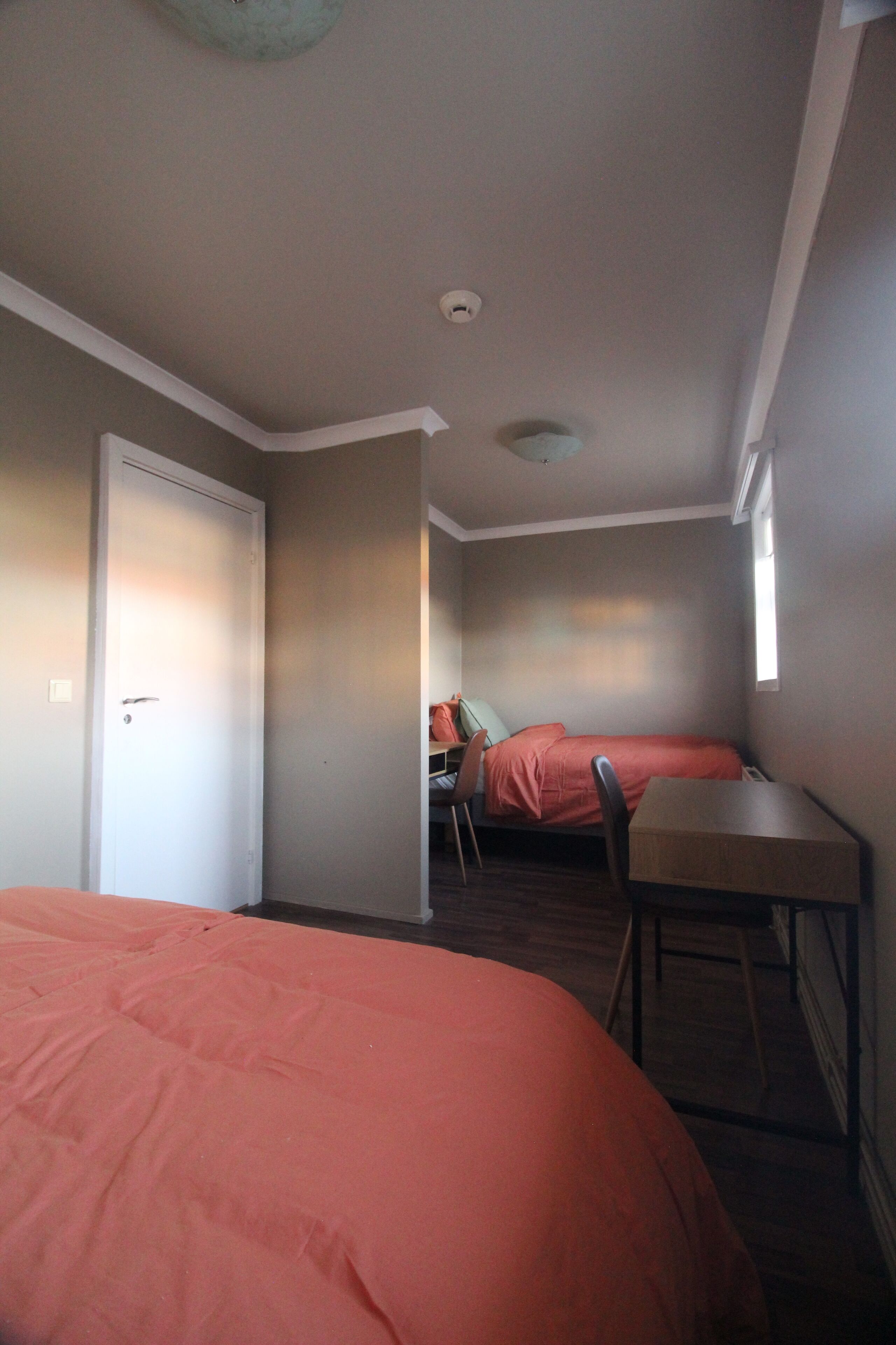 Quarto compacto com duas camas, uma escrivaninha e uma cadeira.
