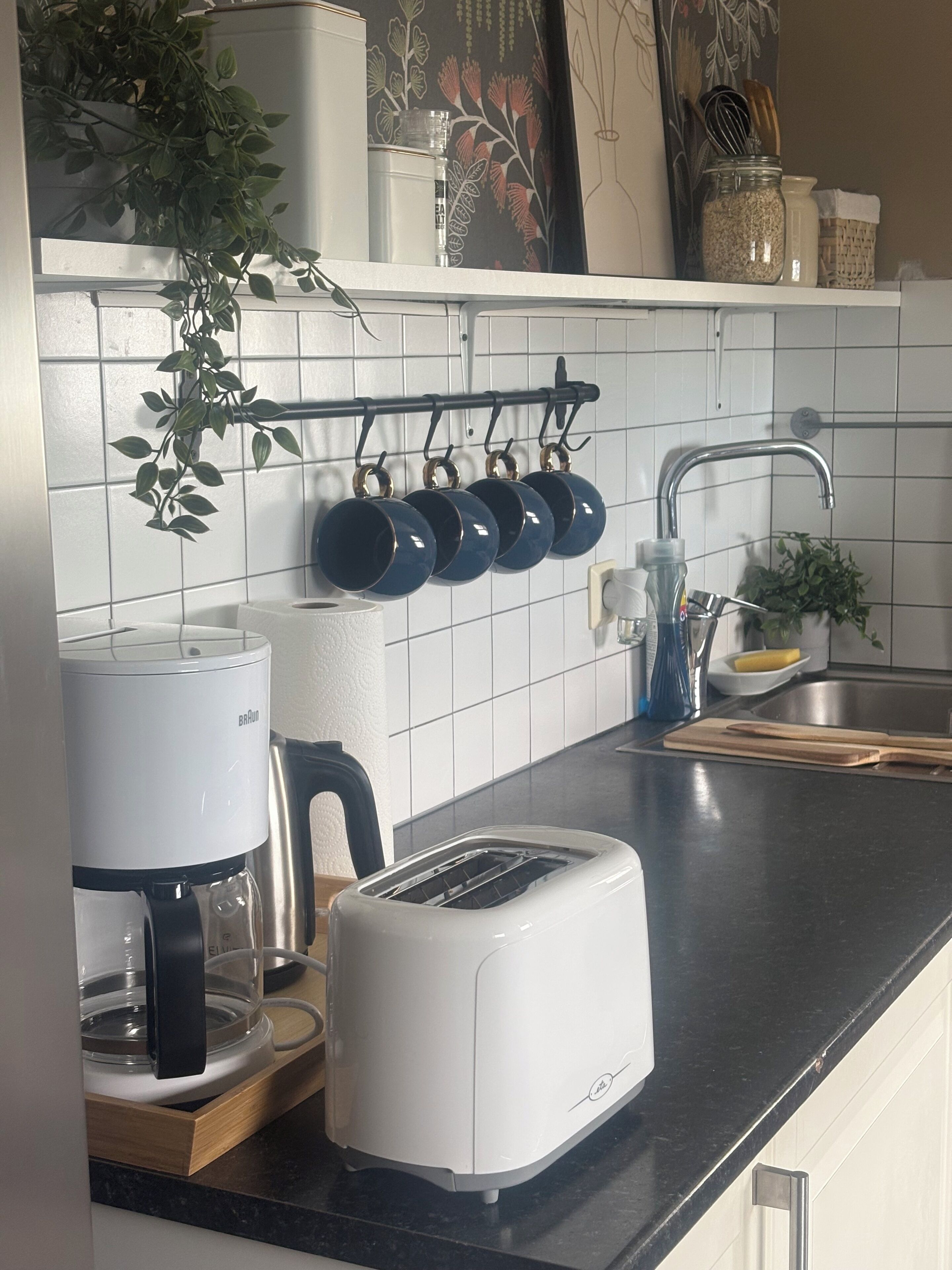 Een keuken met een koffiezetapparaat, broodrooster, hangende pannen en een spoelbak.